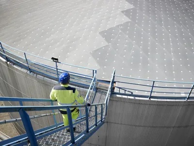 Man in yellow jacket and construction helmet walking down stairs to an oil plant